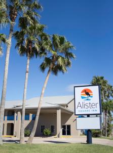 a sign in front of a building with palm trees at Alister Square Inn in Port Aransas