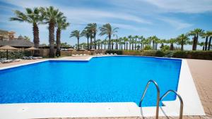 a large blue swimming pool with palm trees in the background at Leo Jardines de Isla Canela in Isla del Moral