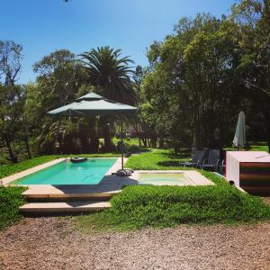 a swimming pool with an umbrella and a table and chairs at Chacra La Escondida in Colonia del Sacramento
