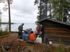a group of people standing around a cabin by the water at Johannisholm Adventure in Johannisholm