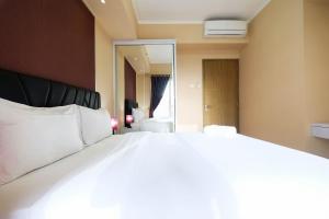 Cette chambre comprend un grand lit blanc et un miroir. dans l'établissement Bright and Stylish 1BR The Oasis Apartment Cikarang By Travelio, à Cikarang