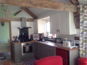 una cocina con armarios blancos y una silla roja en ANVIL COTTAGE en Whitchurch