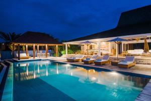 a swimming pool with lounge chairs and umbrellas at night at Villa Tranquilla in Nusa Lembongan