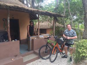 un homme debout devant une maison avec un vélo dans l'établissement Nemasu Eco-lodge, à Gunjur