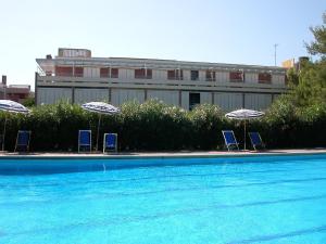 マリーナ・ディ・ビッボーナにあるAppartamenti Marina del Forteのスイミングプールの横の椅子3脚とパラソル