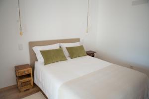 a white bed with two green pillows and a night stand at Casa dos Junqueiros - Countryside Guest House in Caldas da Rainha