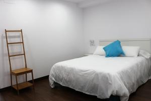 Cama blanca con almohada azul y escalera en Color Suites Alicante, en Alicante