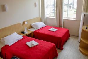 two beds in a hotel room with red sheets at Airam Brasília Hotel in Brasilia