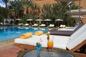 a hotel pool with lounge chairs and a table with drinks at Berbère Palace in Ouarzazate