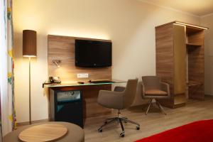 ハノーファーにあるホテル ケーニヒスホフ アム フンクトゥルムのデスク、椅子2脚、テレビが備わる客室です。