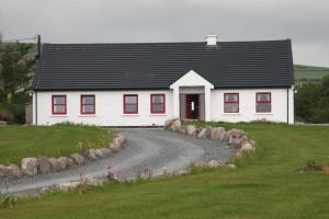 a white house with red windows and a gravel road at Rose cottage in Ballinskelligs