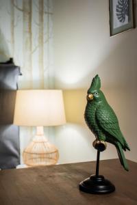 un oiseau vert assis sur une table à côté d'une lampe dans l'établissement Maisons du Monde Hotel & Suites - Nantes, à Nantes