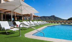 - une rangée de chaises et un parasol à côté de la piscine dans l'établissement Queen Kapiolani Hotel, à Honolulu