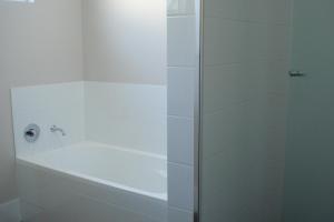 bañera blanca con puerta de ducha de cristal en Railway Cottage, en Bunbury