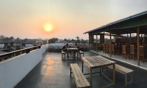 two people sitting at tables on a roof with the sunset at Song of Travel Hostel in Nyaungshwe Township