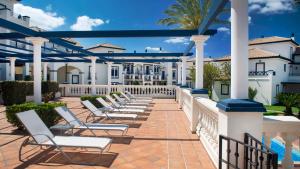 a row of lounge chairs on a patio with white buildings at Leo San Bruno in Isla Canela