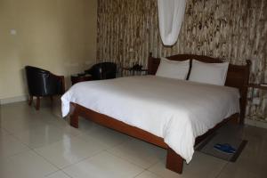 a bedroom with a large bed with white sheets and chairs at The Garden Place Hotel in Ruhengeri