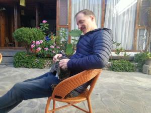 un homme assis sur une chaise avec un chat dans l'établissement Log Cabin, à Dali