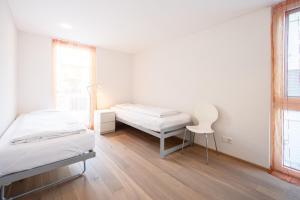 a white room with two beds and a chair at Casa Mutta in Laax