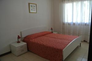 a bedroom with a bed with a red bedspread and a window at Condominio LISA in Lignano Sabbiadoro