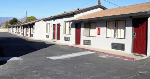 a white building with red doors and a parking lot at Palm Inn Motel - Montclair in Montclair