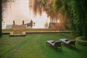 due panche sedute sull'erba vicino a un corpo d'acqua di Chittoor Kottaram Royal Mansion- CGH Earth a Cochin