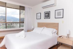 a white bedroom with a large white bed and a window at Aptos Alcazar Oviedo By HOUSY HOST in Medellín