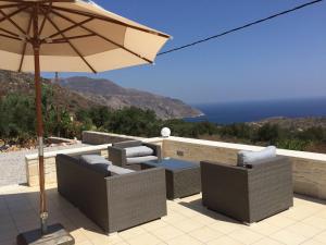 a patio with chairs and an umbrella and the ocean at Villa Anatoli in Epáno Kefalás