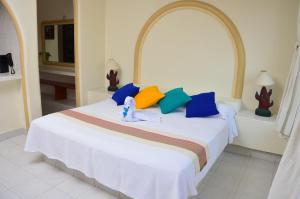 1 dormitorio con cama blanca y almohadas coloridas en Arena Suites en Zihuatanejo