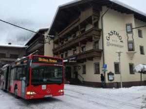 Przed budynkiem stoi czerwony autobus. w obiekcie Hotel Untermetzger w mieście Zell am Ziller