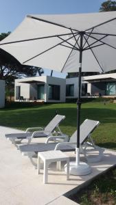 a row of white lounge chairs and an umbrella at Casa Rio da Prata in Aldeia do Meco