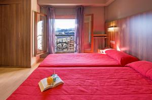 Un dormitorio con una gran cama roja con un libro. en Hotel Avenida, en La Seu d'Urgell