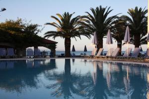 a swimming pool with chairs and palm trees and the ocean at Zakantha Beach in Argassi