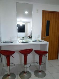 una cocina con encimera blanca con taburetes rojos en APT 2 quartos da Doris Monteiro, en Maceió