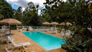 a swimming pool with white chairs and umbrellas at Hotel Fazenda dos Anjos in Cambuquira