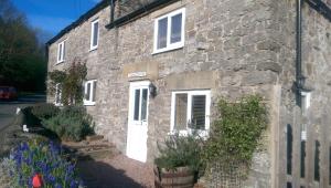 a stone house with a white door and some plants at Hillocks Cottage, Kniveton in Kniveton