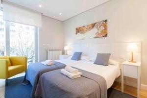 a bedroom with two beds and a yellow chair at The Rentals Collection | Alday in San Sebastián