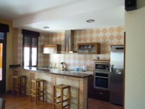 a kitchen with a counter with stools and a refrigerator at CASA RURAL LOS POCICOS in San Carlos del Valle