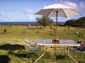 a table with an umbrella in a field with chairs at Cabañas Krava Inn in Hanga Roa