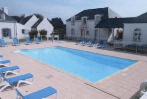 une grande piscine avec des chaises bleues et une maison dans l'établissement Résidence Marie Galante Locmaria avec piscine, à Locmaria