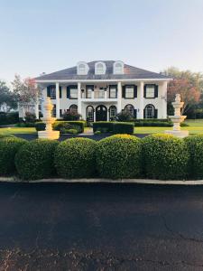 una grande casa bianca con cespugli di fronte di The Plantation House Boutique Inn a Pflugerville