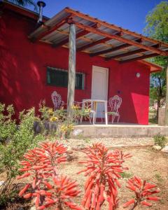 a red house with a table and chairs in front of it at Cabañas Los Algarrobos in San Marcos Sierras