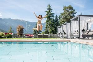 Eine Frau, die in die Luft springt, neben einem Pool in der Unterkunft Hotel Waldhof in Percha