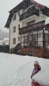 a child standing in the snow in front of a house at Csaki Vendeghaz in Sovata