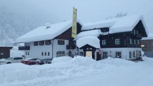 a building covered in snow with cars parked in front at Pension Backstuba in Partenen