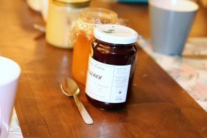 a jar of honey on a wooden table with a spoon at Le Cairn Chambres & Table d'hôtes in Saint-Bonnet-en-Champsaur