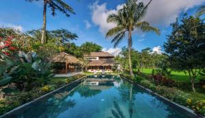a swimming pool in front of a house with palm trees at Villa Arcadia in Gianyar