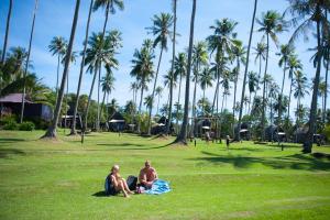 dos personas sentadas en el césped en un parque con palmeras en Koh Kood Beach Resort, en Ko Kood