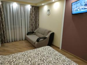 Cette chambre comprend un lit, une chaise et une télévision. dans l'établissement Apartments in the Center Maidan, à Rivne
