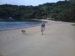 uma mulher a passear na praia com um cão em Apartamendo na Enseada em Ubatuba